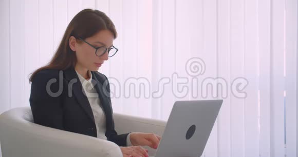 特写侧景照片年轻的白种人女商人戴着眼镜在笔记本电脑上工作看着镜头微笑视频的预览图