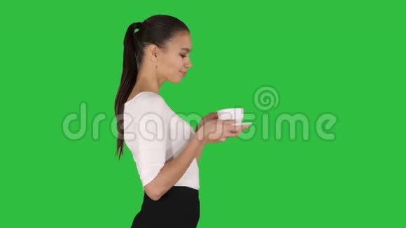 美丽的黑发女人带着白色的杯子茶或咖啡走在绿色的屏幕上铬钥匙视频的预览图