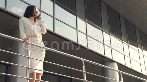 在城市里一位穿着白色衬衫和裙子的漂亮黑发商务女性用智能手机慢镜头拍摄视频的预览图