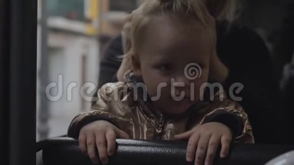 一个穿着金色夹克的女婴坐在公共汽车上的母亲腿上视频的预览图
