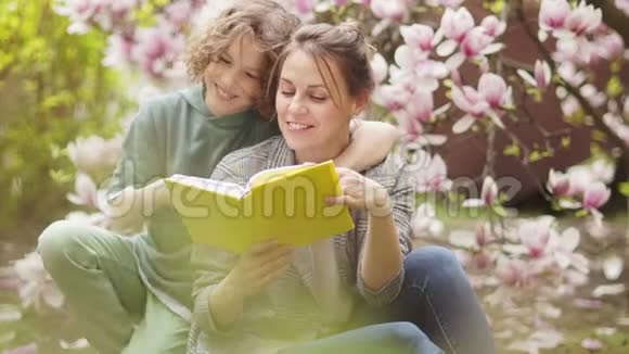 春天的母子画像一个抱着一本书的女人抱着一个卷曲的少年背景是视频的预览图