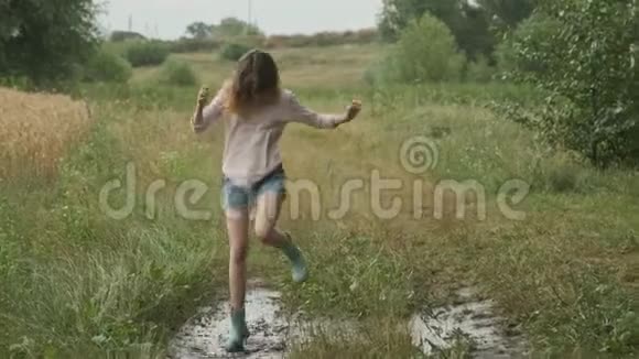 美丽的微笑少女在乡间小路上的泥泞的水坑中跳跃视频的预览图