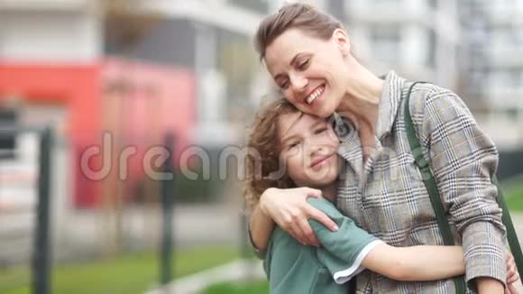 成熟的漂亮女人在一条城市街道的中间拥抱她卷曲的十几岁的儿子家庭幸福母亲节视频的预览图