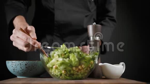 男人把素食的绿色沙拉和深色背景的木勺混合在一起视频的预览图