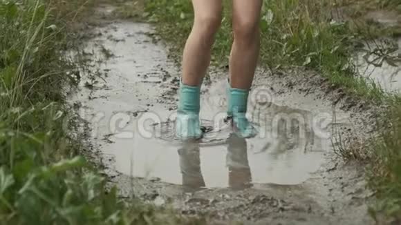 美丽的微笑少女在乡间小路上的泥泞的水坑中跳跃视频的预览图