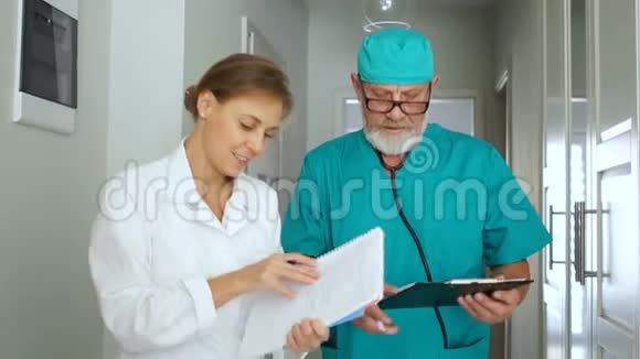 一位有经验的医生和他的医疗助理在诊所的走廊里交谈医务人员医生工作日视频的预览图