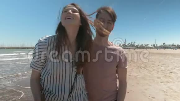 一对微笑的夫妇在阳光明媚的日子里沿着海滩散步视频的预览图