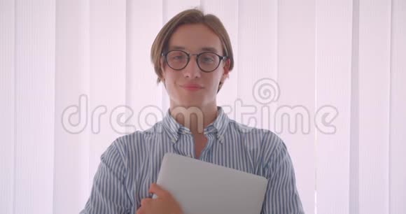 年轻英俊的白种人商人戴着眼镜手持笔记本电脑幸福地站在室内视频的预览图