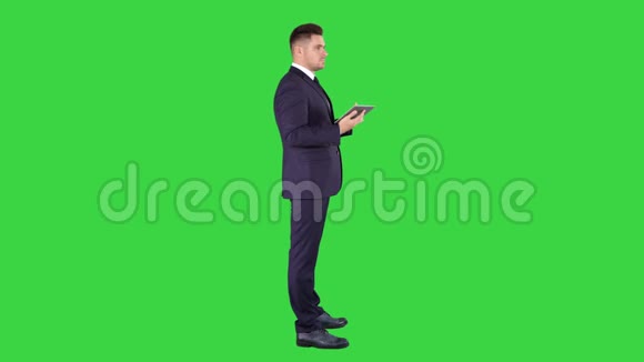 年轻的商人触摸数字平板电脑和检查对象在他前面的绿色屏幕铬键视频的预览图