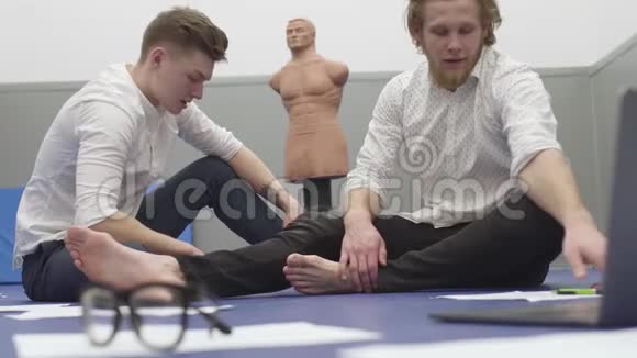 两个男人坐在健身房的地板上前面的文件和眼镜假人是他们的背景有胡子的家伙视频的预览图