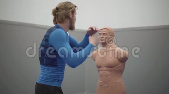 长胡子的职业男子有着运动的身体和金色的长发在健身房里与一个鲍勃盒的人体模型做侧弯视频的预览图