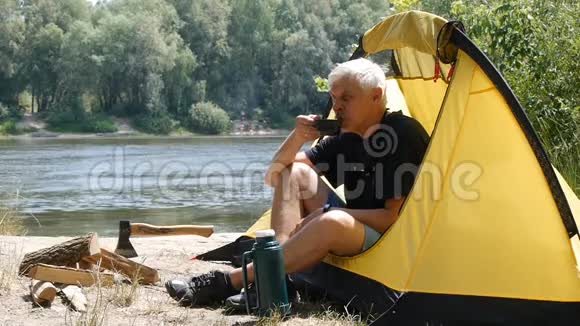 徒步旅行者坐在帐篷里露营者喝咖啡或茶河流和森林的背景放松旅行视频的预览图
