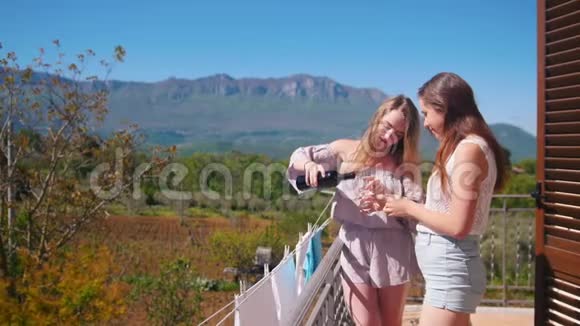 两个年轻的女人站在阳台上在酒杯里倒酒视频的预览图