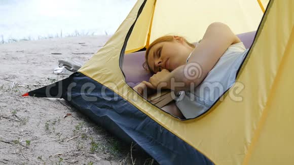 年轻的女旅行者睡在帐篷里疲惫的徒步旅行者女孩在露营帐篷里拿着一本书睡着了徒步旅行旅游绿色视频的预览图