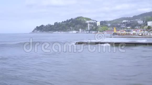 防波堤上有泡沫破裂的小海浪鸟瞰度假小镇背景山脉海滩季节海岸景观视频的预览图