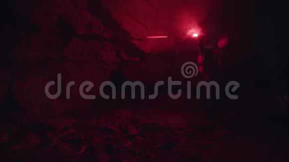洞穴黑暗中的石头上有红色燃烧信号的人剪影极端的旅游理念视频的预览图