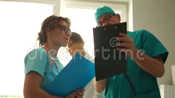 医生给助手指示成熟的男人和年轻的女人穿着医用长袍站着说话视频的预览图
