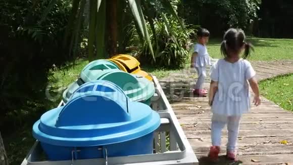 亚洲小女孩把空塑料瓶扔进公园的回收垃圾桶视频的预览图