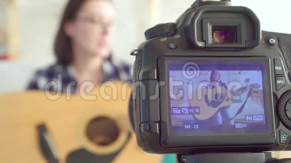 年轻女性博客作者坐在沙发上弹吉他透过镜头屏幕视频的预览图