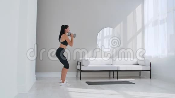 一个身材健壮身材匀称的漂亮女孩正在明亮宽敞的客厅里做蹲式练习里面有视频的预览图