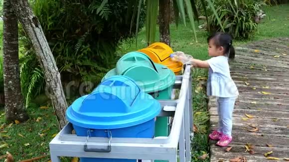 亚洲小女孩把空塑料瓶扔进公园的回收垃圾桶视频的预览图