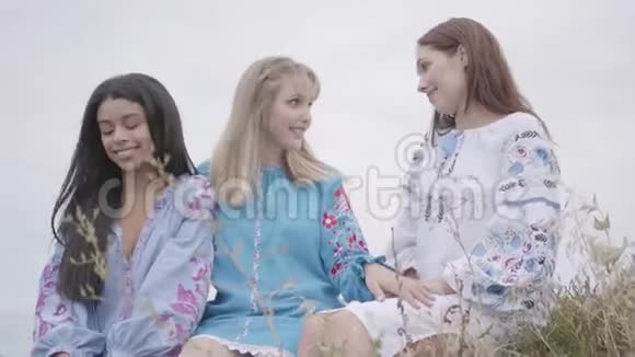 三位身穿夏季时装长裙的年轻女友在赛场上交谈两个高加索女孩和一个非洲女孩视频的预览图