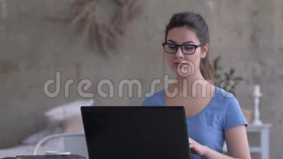 戴眼镜的商务女孩在家工作坐在手提电脑上打字看着屏幕特写视频的预览图
