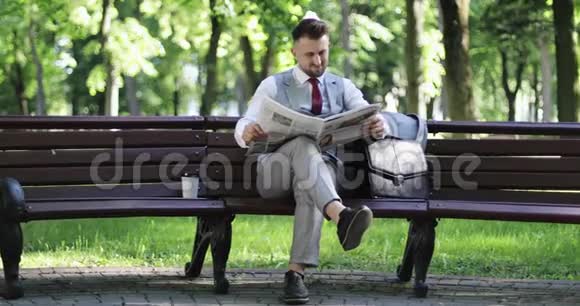 一位留着胡子的英俊商人正坐在公园里看报纸视频的预览图