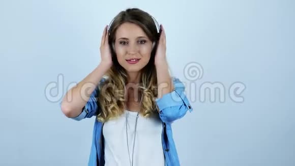 年轻漂亮的性感金发女郎戴着白色背景耳机欣赏最喜欢的歌曲视频的预览图