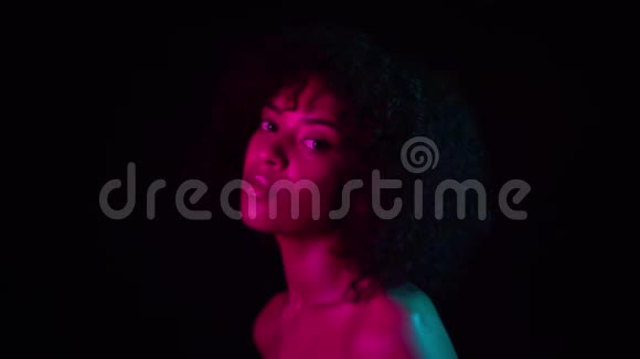 黑色背景下粉红色霓虹灯下年轻迷人的非洲女孩的肖像妆容完美诱人的女人视频的预览图