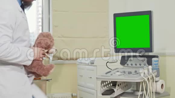 儿科医生抱着泰迪熊背着绿色屏幕的超声波扫描仪视频的预览图