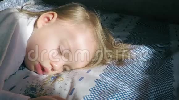 美丽的小女孩金发睡在床上被阳光照亮阳光覆盖着一条米色的毯子视频的预览图