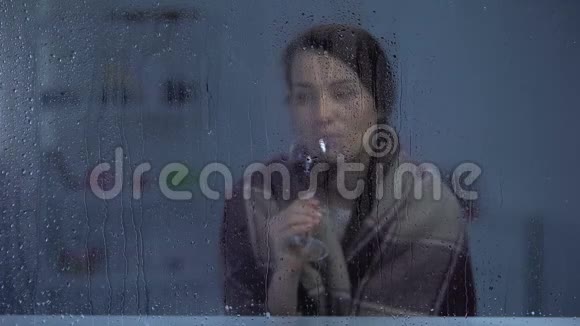 穿着毛毯的女人在雨窗后喝着酒寒冷的夜晚视频的预览图
