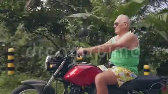 成熟的人骑摩托车在热带乡村的青山和热带雨林景观上旅行高级官员视频的预览图