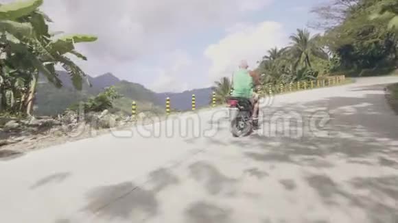 在青山覆盖热带雨林的蜿蜒公路上驾驶摩托车的老人成人男子旅行视频的预览图