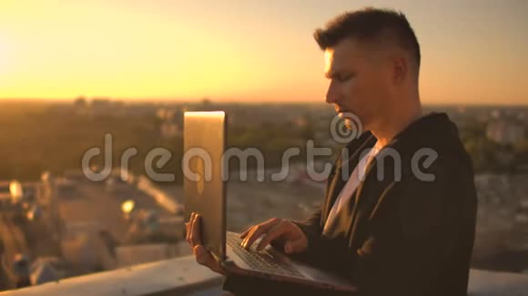 一个有笔记本电脑的程序员坐在屋顶上在日落时写代码远程工作自由职业者工作自由打字视频的预览图