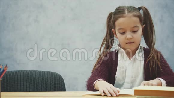 小女孩读一本书坐在灰色的内部学习教科书的女学生穿校服的孩子视频的预览图