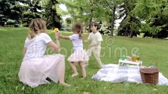快乐的妈妈和她的两个孩子一起玩在户外吹肥皂泡视频的预览图