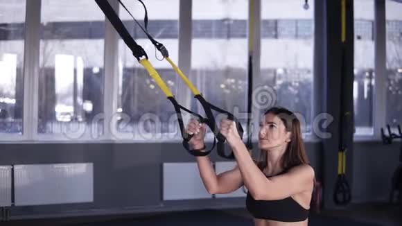 在健身俱乐部或健身房里长头发的运动妇女用悬吊带锻炼深蹲重量视频的预览图