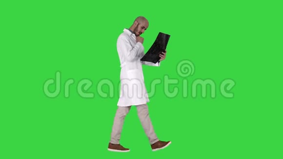 年轻的男医生在绿色屏幕上行走时阅读和复习MRI脑扫描Chroma键视频的预览图