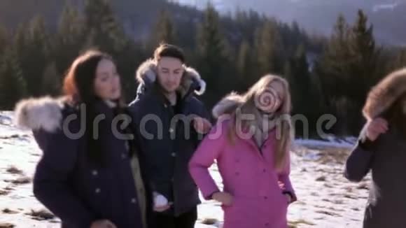 在一个阳光明媚的冬日三个女孩和一个男孩在针叶林的背景下在山上休息视频的预览图
