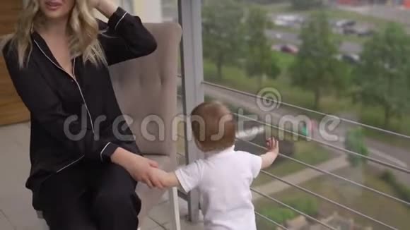 在阳台上玩年轻的金发母亲在家里和她的小儿子一起度过美好的时光穿着平的衣服视频的预览图