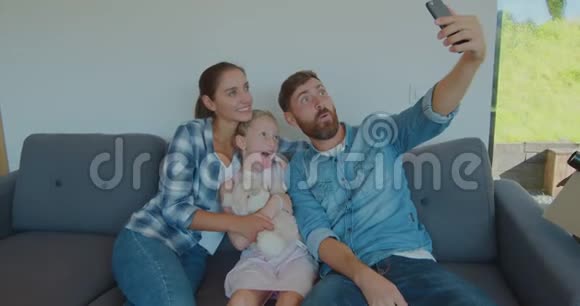 美丽的家庭在智能手机上做令人难忘的自拍同时放松一次又一次地坐在纸板箱之间视频的预览图