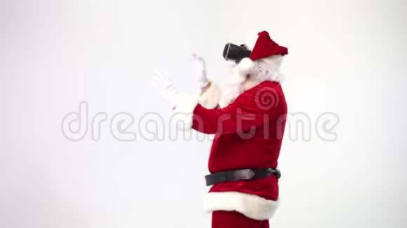 圣诞节圣诞老人在白色背景上戴着虚拟现实眼镜工作时带着信息挥动着他的手VR视频的预览图