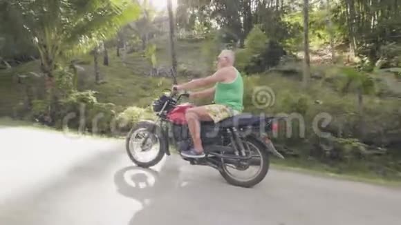 在绿色高地景观热带公路上骑摩托车的成年男子一个骑摩托车的退休老人视频的预览图