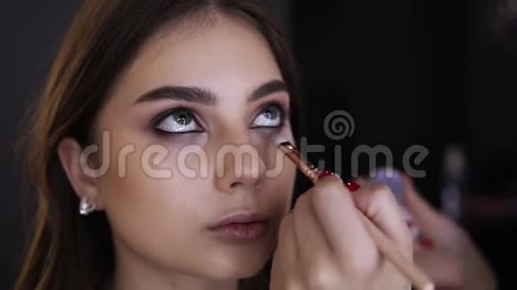 化妆室化妆眼睛的年轻女人的肖像化妆师用刷子将明亮的眼影涂在低处视频的预览图