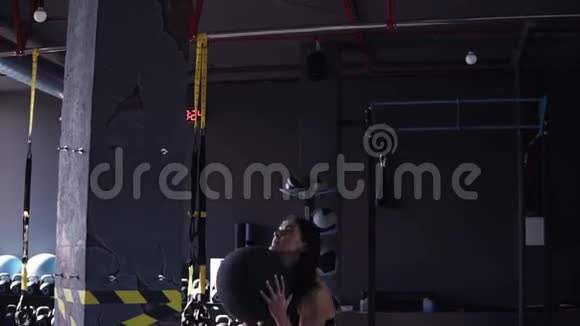 侧视镜头一名身穿黑色背风和胸罩的年轻健康女子将一个药球抛向一个对手视频的预览图