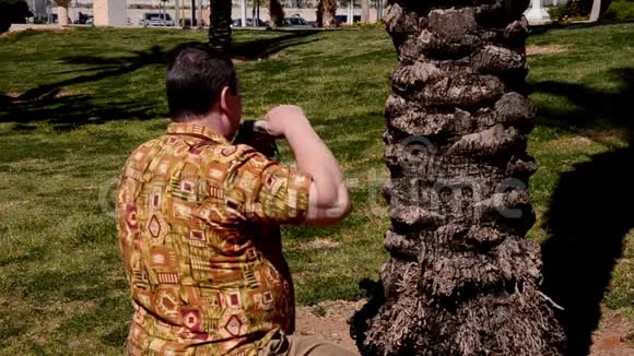 穿着阿洛哈衫的男人在城市公园用复古相机拍照视频的预览图