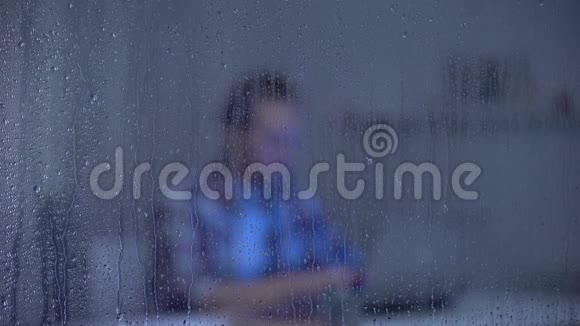 一个在雨窗后深夜工作在笔记本电脑上的疲惫男人自由职业视频的预览图