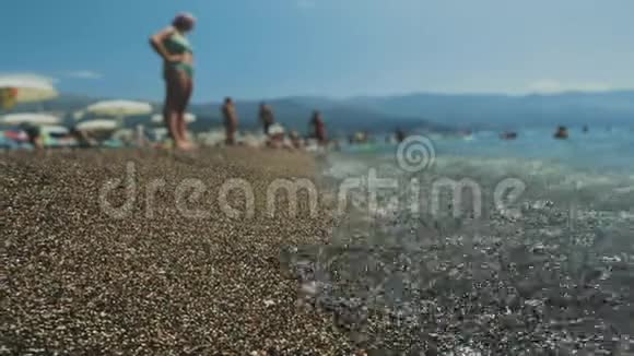 人们游客在度假小镇的鹅卵石海滩上放松炎热的夏天度假浪打岸上山区视频的预览图